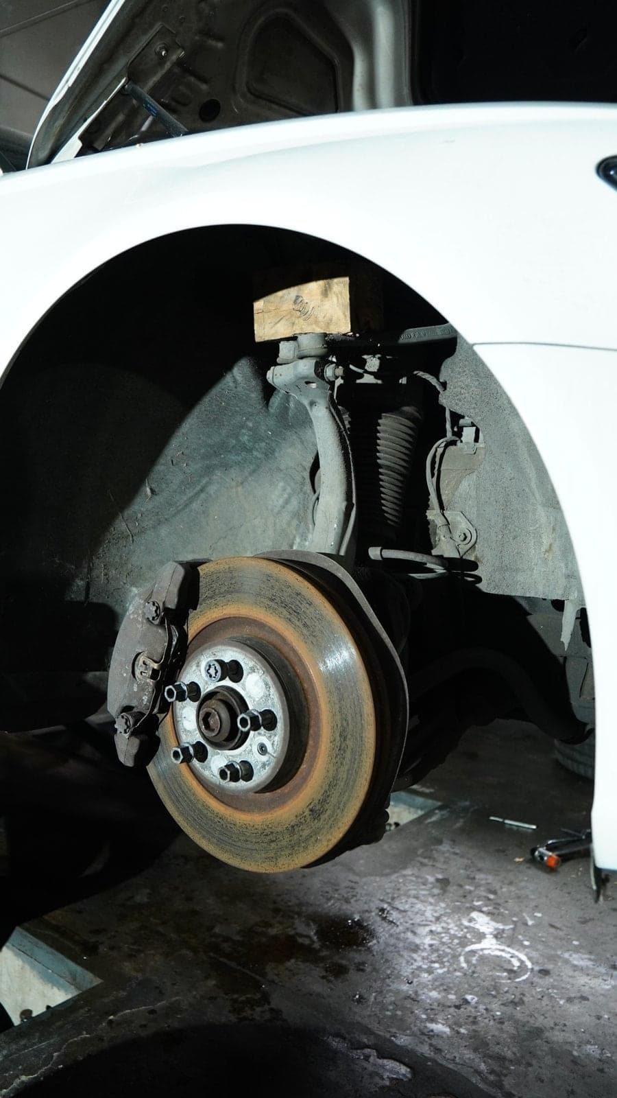 Coilover strut and brake disc in the front wheel well of a white Audi A6 with the wheel off