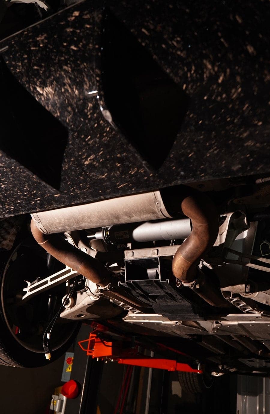 Underside of a raised SUV showing a forged carbon diffuser, exhaust pipes and rear suspension