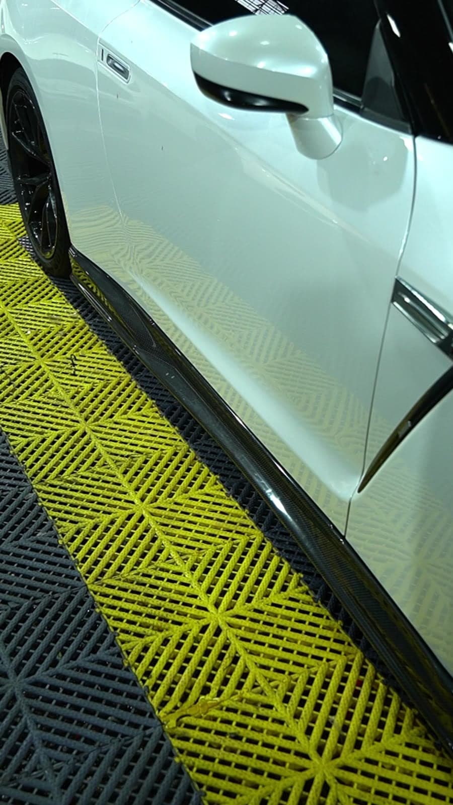 Carbon fibre side skirt fitted to a white Nissan GT-R on yellow workshop floor tiles