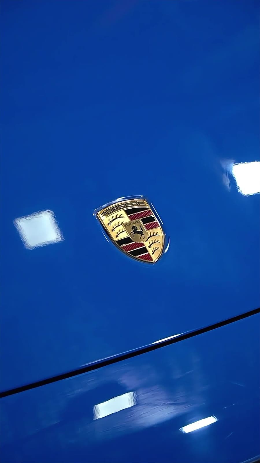 Porsche crest on a glossy blue bonnet after paint protection film installation