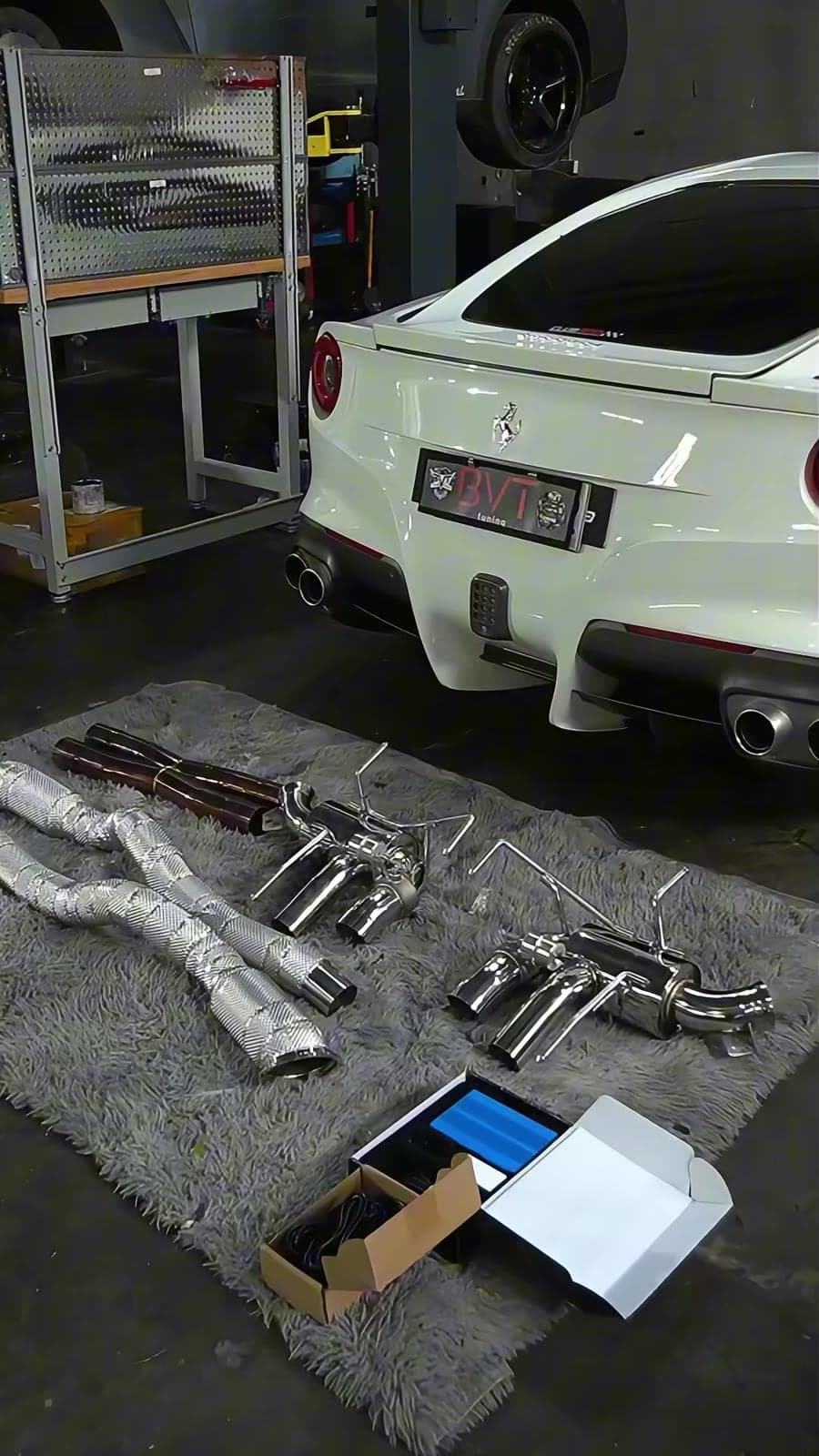 Valved exhaust system laid out on a rug behind a white Ferrari F12berlinetta