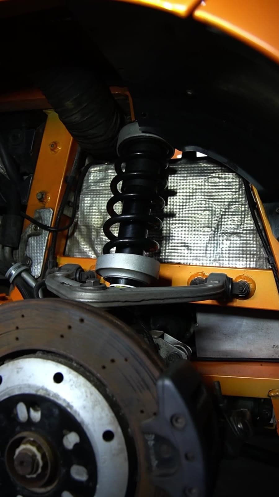 Coilover damper and upper wishbone inside the orange wheel well of a supercar with the wheel removed