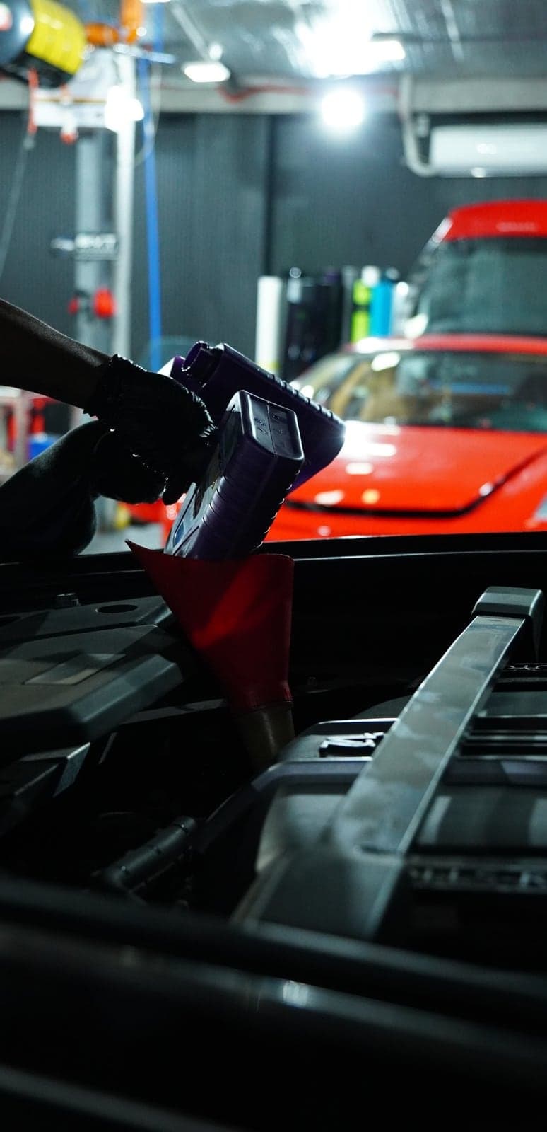 Fresh engine oil poured through a red funnel during a preventive maintenance service