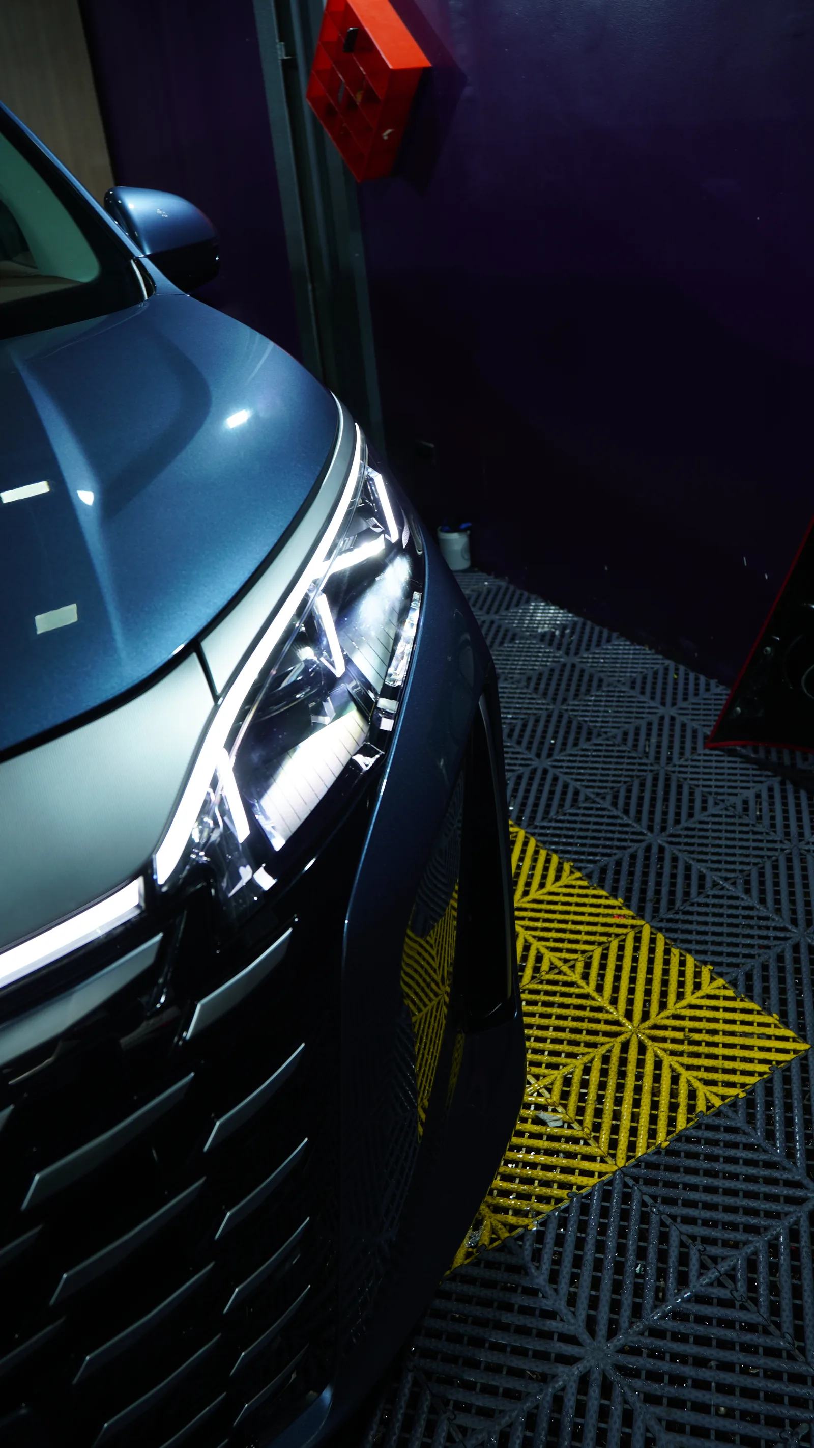 Headlight and glossy bonnet of a blue-grey BYD eMAX 9 after paint protection film in the PPF bay