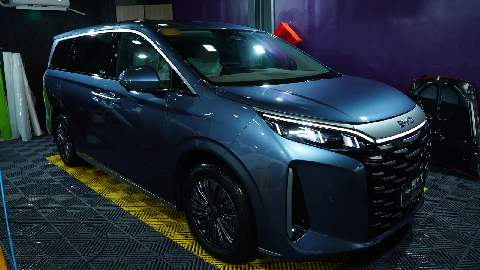 Blue-grey BYD eMAX 9 front three-quarter view in the BVT PPF bay