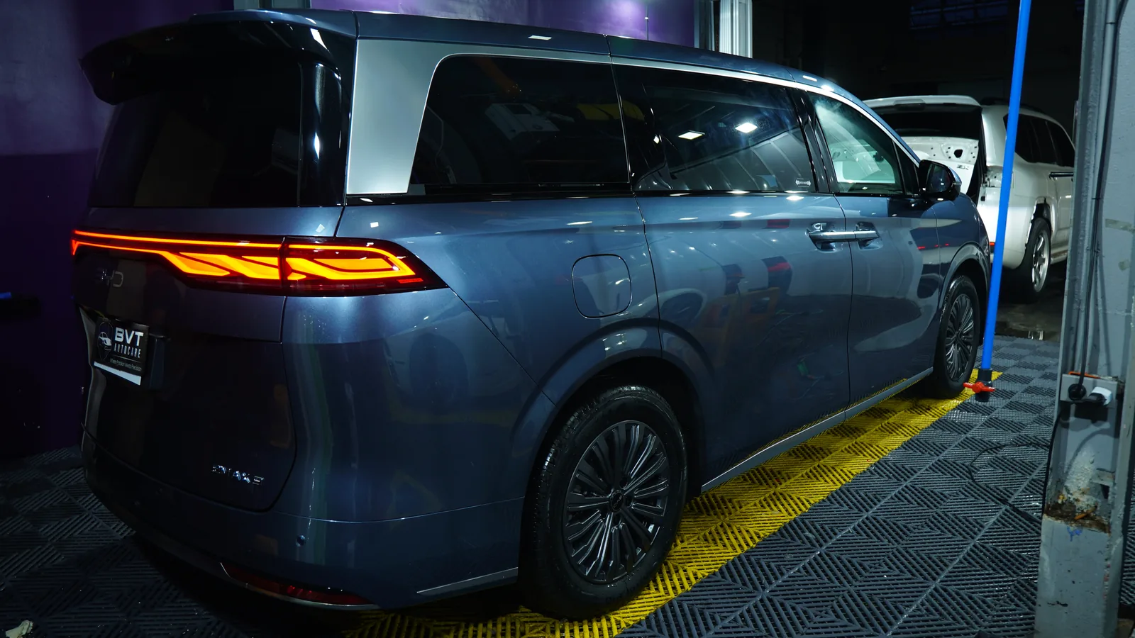 Rear three-quarter view of the blue-grey BYD eMAX 9 in the PPF bay with its light bar on