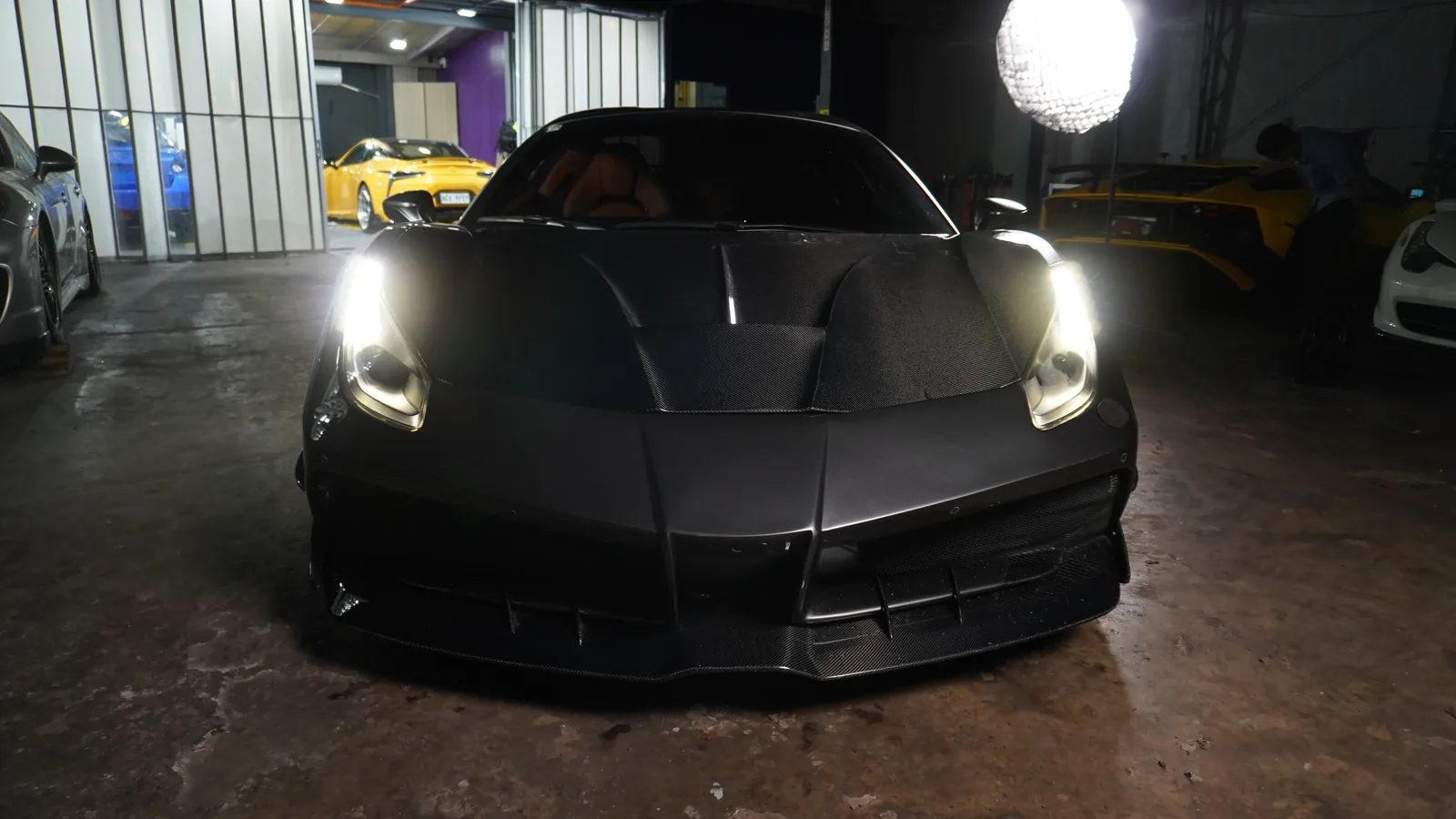 Matte grey Ferrari 488 Spyder with its carbon body kit, headlights on, in the BVT workshop
