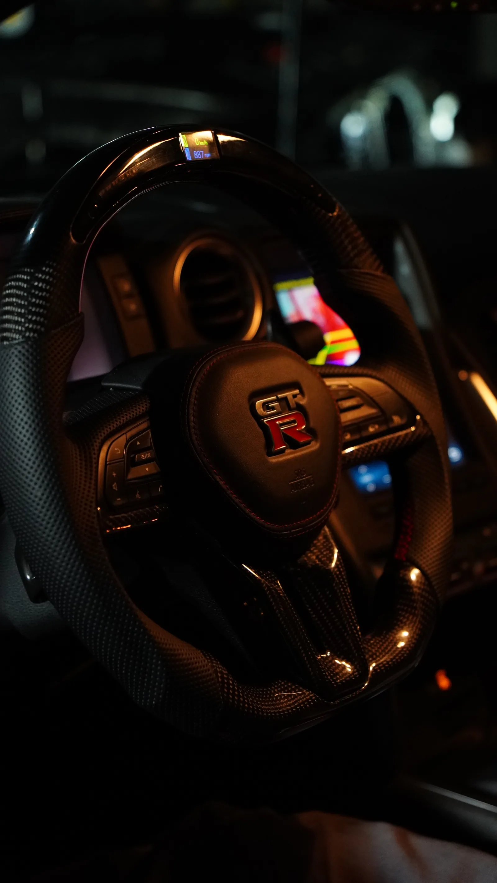 Nissan GT-R R35 carbon steering wheel with the GT-R badge and coloured switches, in warm light