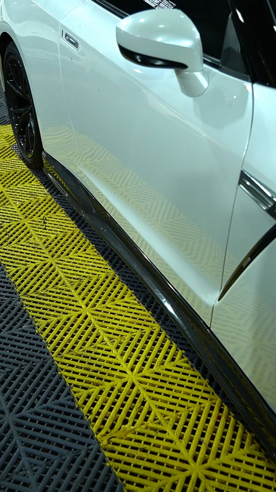 Carbon fibre side skirt fitted to a white Nissan GT-R R35 on the yellow workshop floor tiles