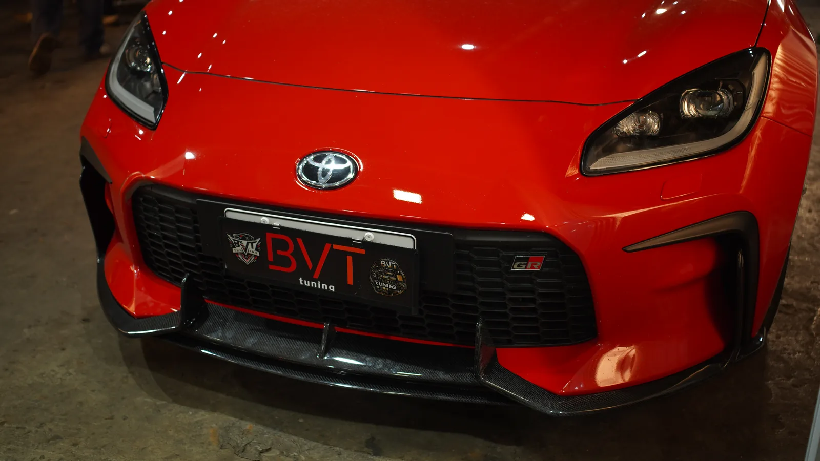 Front bumper of the red Toyota GR86 with the carbon lip and canards below the BVT Tuning plate