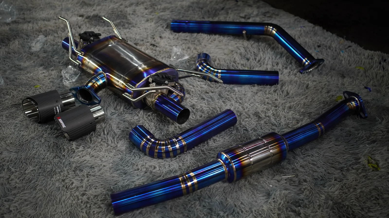 Titanium exhaust system with burnt-blue pipes and carbon tips laid out before fitting to the Toyota GR86
