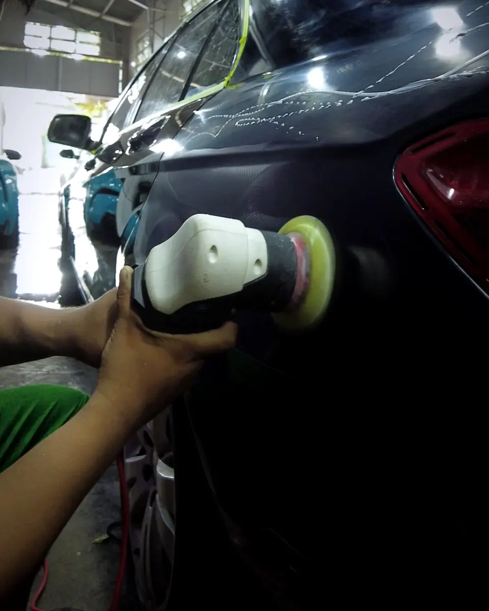 Machine polisher on the paint of a dark blue sedan