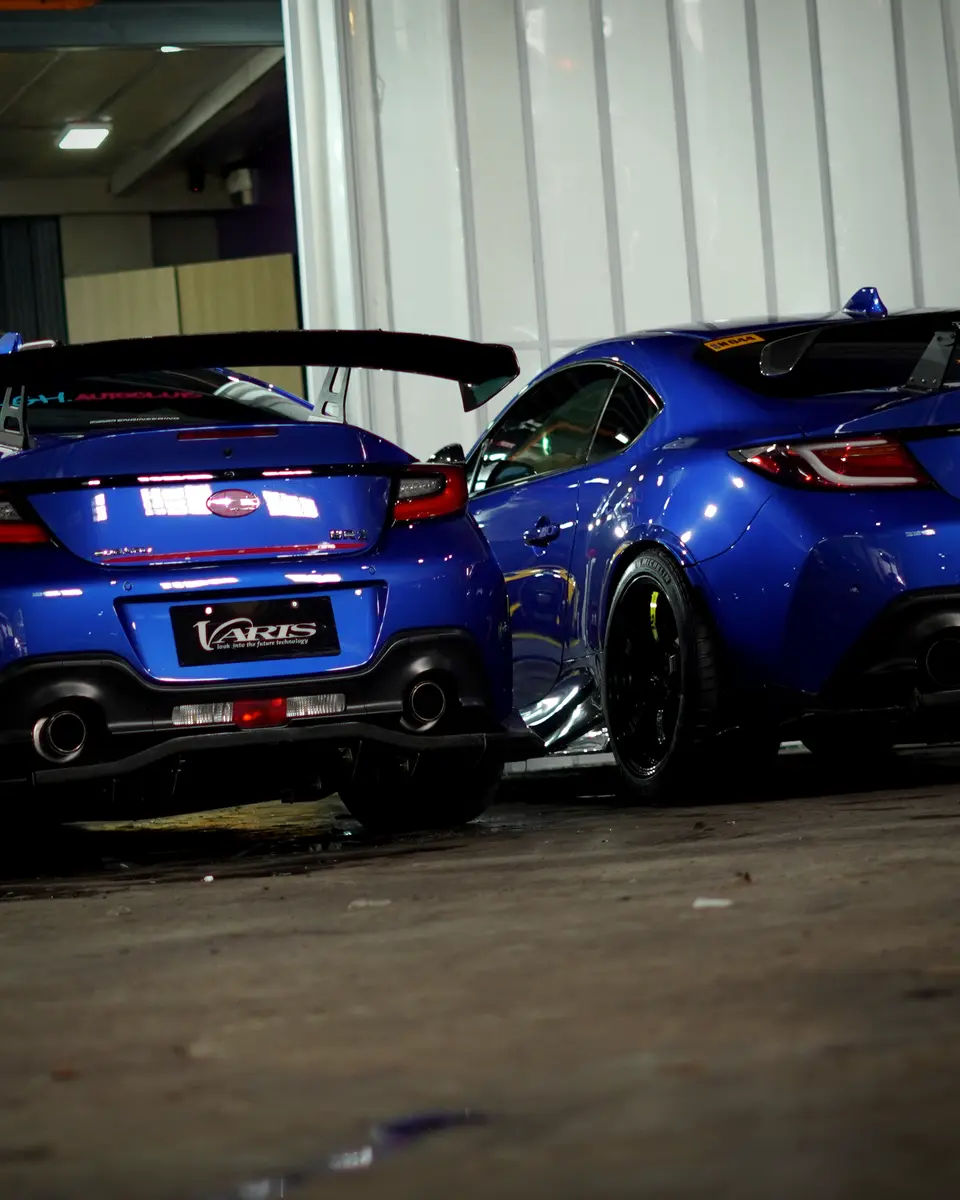 Two blue Subaru BRZs with aero parts in the workshop